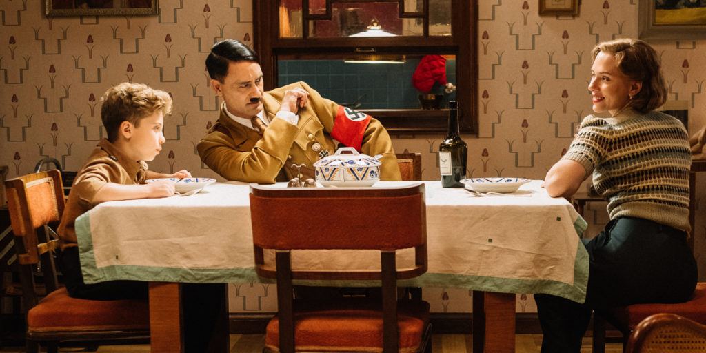 First still from the set of WW2 satire, JOJO RABIT. (From L-R): Jojo (Roman Griffin Davis) has dinner with his imaginary friend Adolf (Writer/Director Taika Waititi), and his mother, Rosie (Scarlet Johansson). Photo by Kimberley French. © 2018 Twentieth Century Fox Film Corporation All Rights Reserved